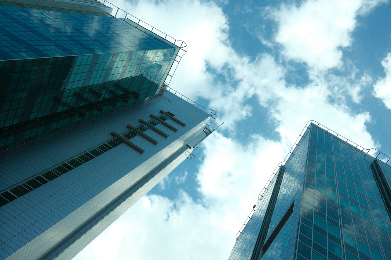Low angle view of modern glass skyscrapers with clouds reflecting, under a bright blue sky.