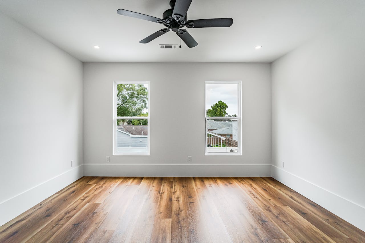 Modern minimalist bedroom featuring a ceiling fan and natural light from two windows in New Orleans.